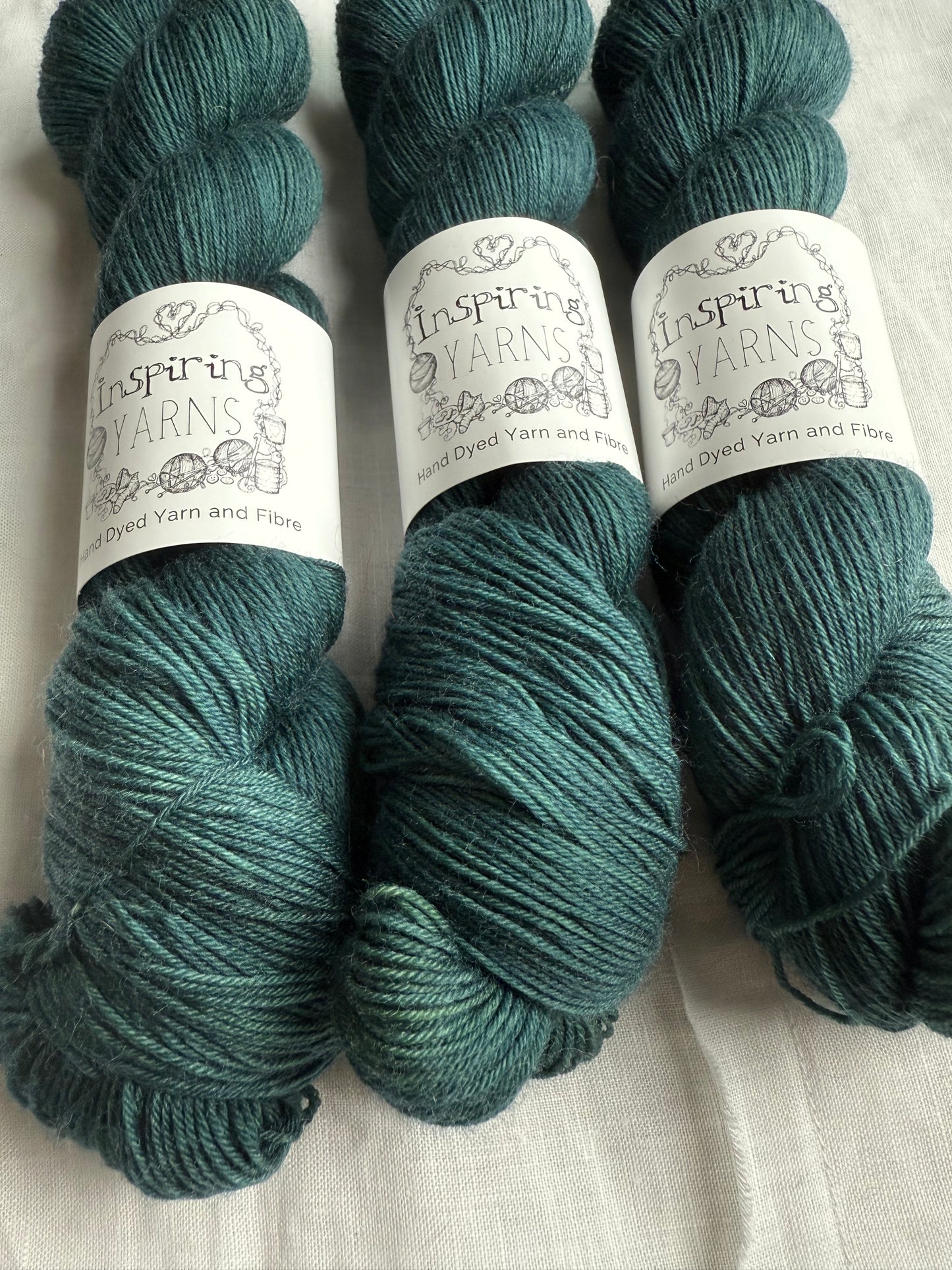 Three skeins of blue/green yarn with white inspiring yarns labels on a white background