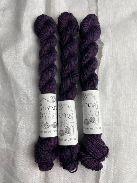 Three mini skeins of dark purple Merino Smooth Sock yarn labelled Inspiring Yarns on a white linen background.