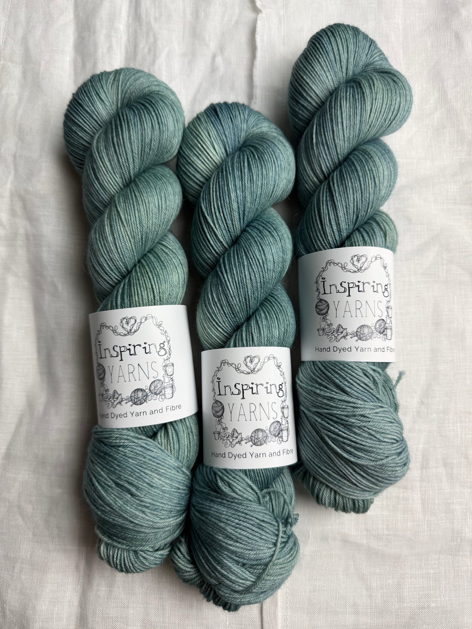 Three skeins of teal yarn with 'Inspiring Yarns' labels on a white background