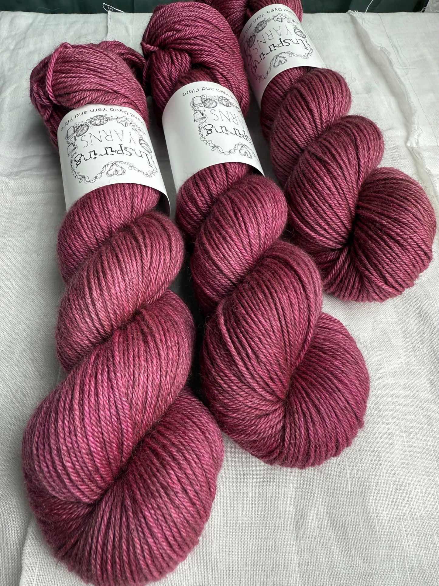 Three skeins of pink yarn with labels on a white fabric background. 