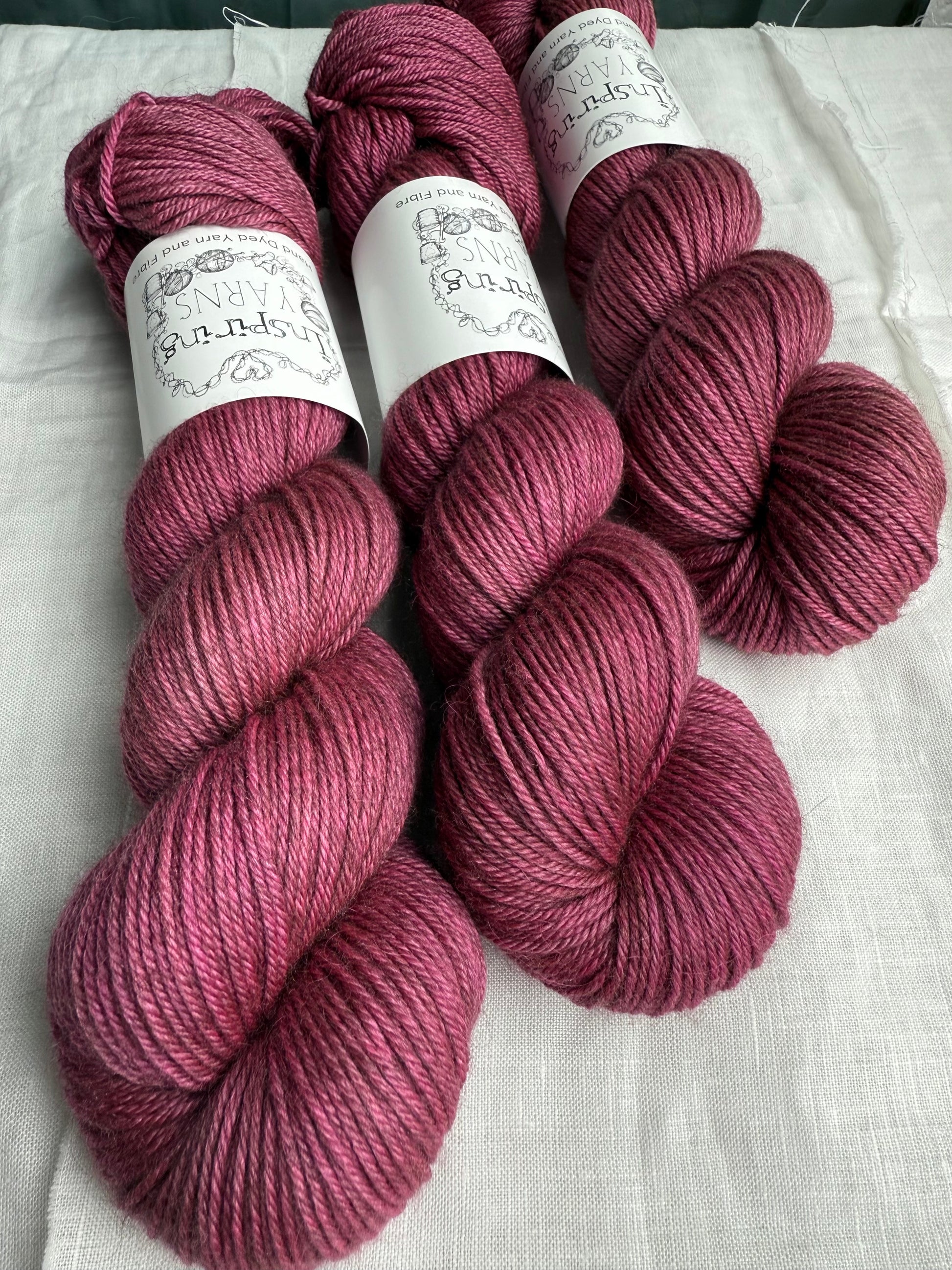 Three skeins of pink yarn with labels on a white fabric background. 