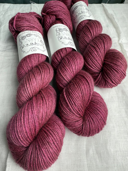 Three skeins of pink yarn with labels on a white fabric background. 