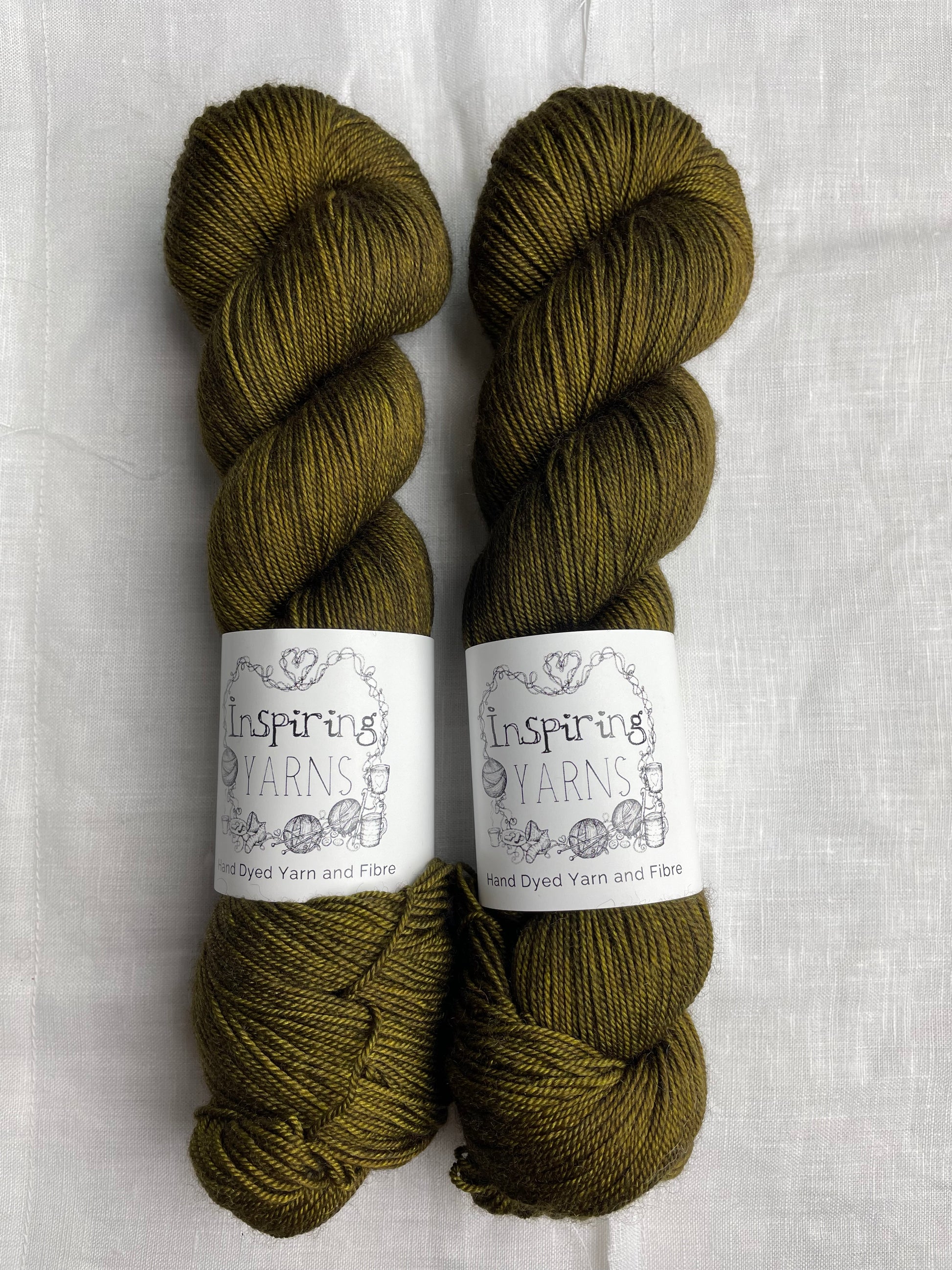 Two tonal dark olive green coloured skeins of hand dyed Yak Silk 4Ply yarn branded Inspiring Yarns on a white linen background.