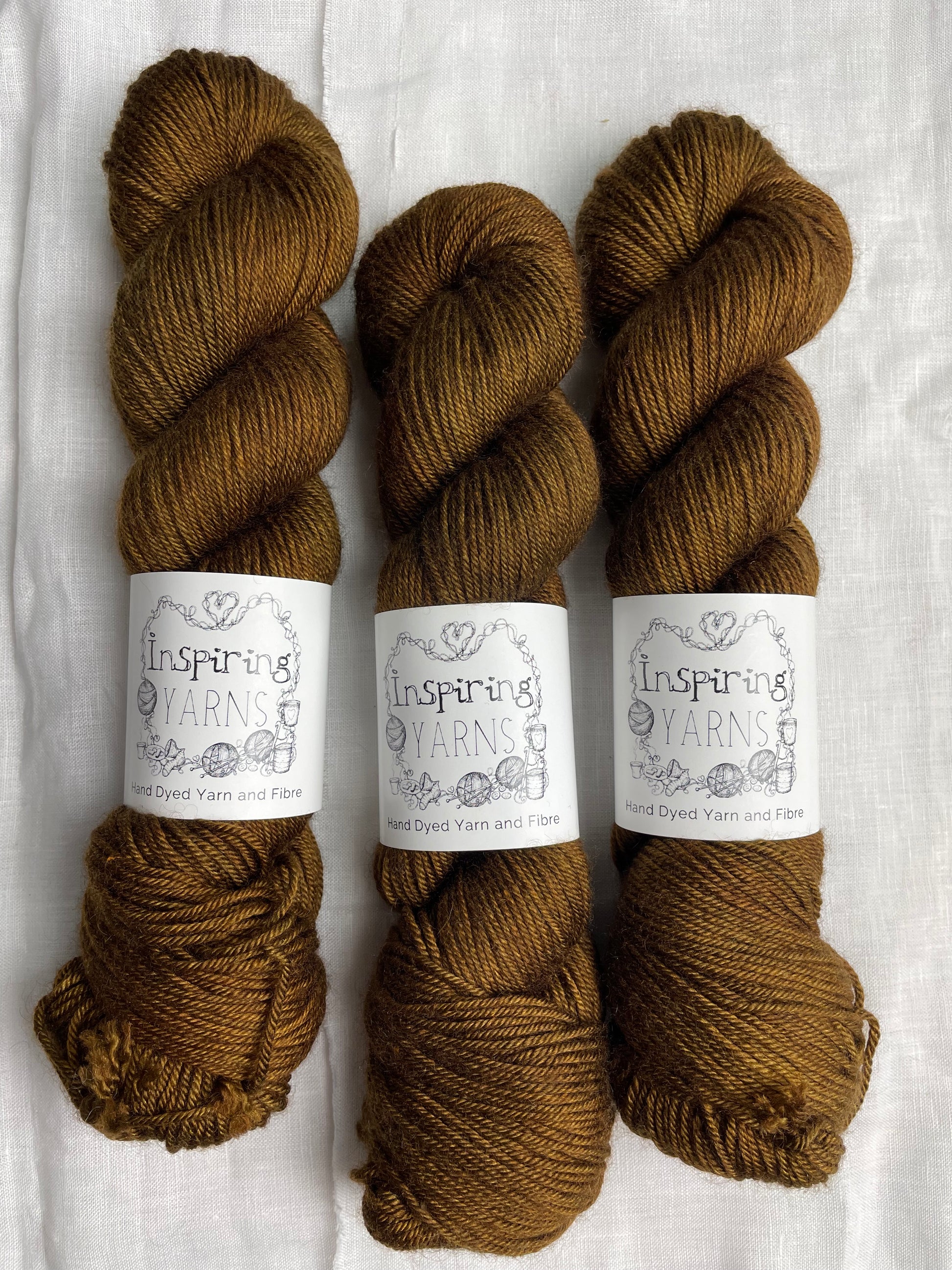 Three skeins of bronze brown coloured yak silk dk yarn branded Inspiring Yarns on a white linen background.