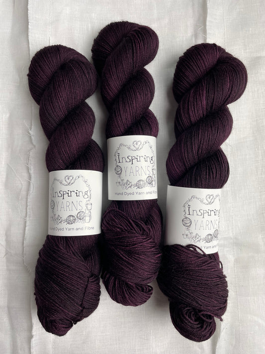 Three skeins of merino smooth sock yarn in a tonal dark burgundy colour labelled Inspiring Yarns on a white linen background. 