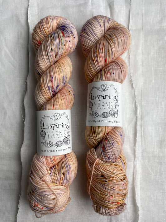 Two speckled peach coloured skeins of Merino Smooth Sock yarn branded  Inspiring Yarns on a white linen fabric background. 