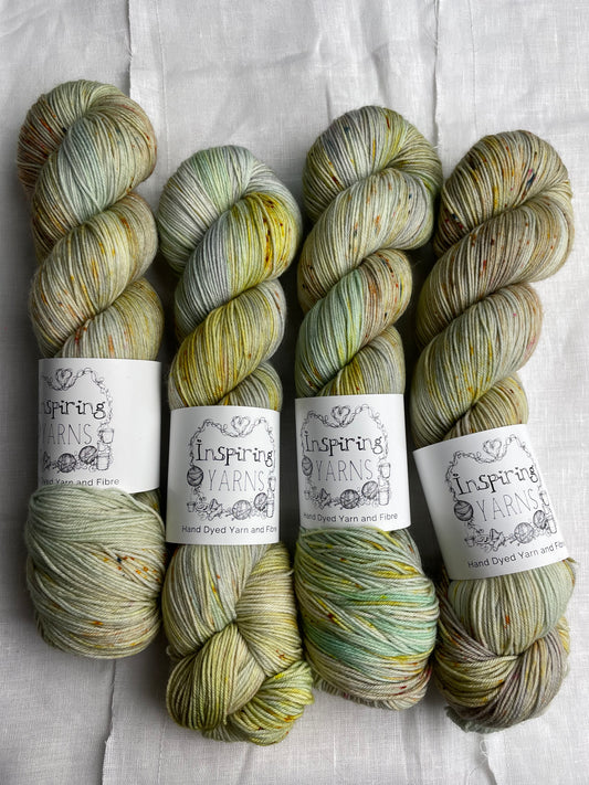 Four lightly speckled, variegated grey and green coloured skeins of Merino Smooth Sock yarn branded  Inspiring Yarns on a white linen fabric background. 