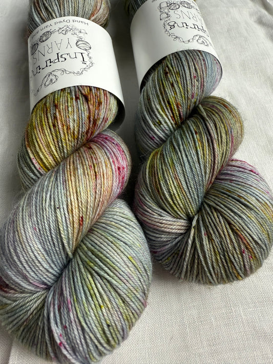 Three skeins of  grey yarn with speckles of green brown red with visible labels on a textured surface.