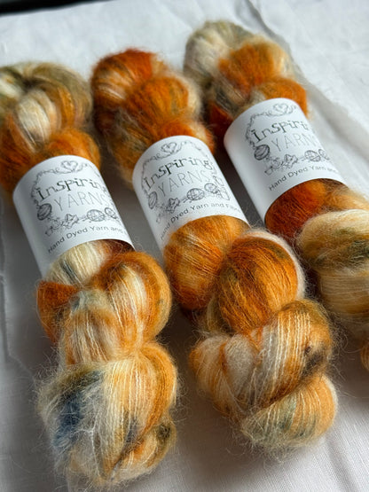 Three skeins of orange and beige yarn at an angle with inspiring yarns labels on a white background.