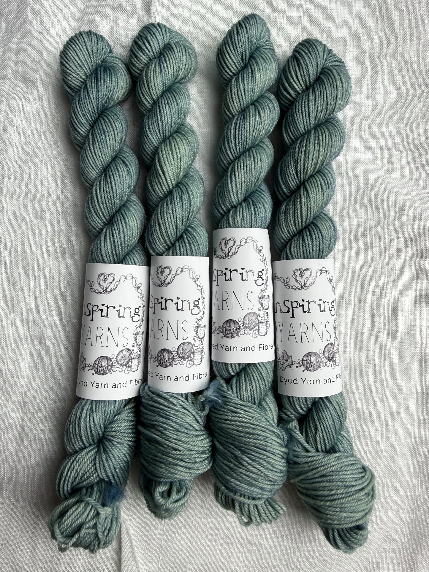 Four skeins of yarn in a teal colour with 'Inspiring Yarns' labels on a white background.