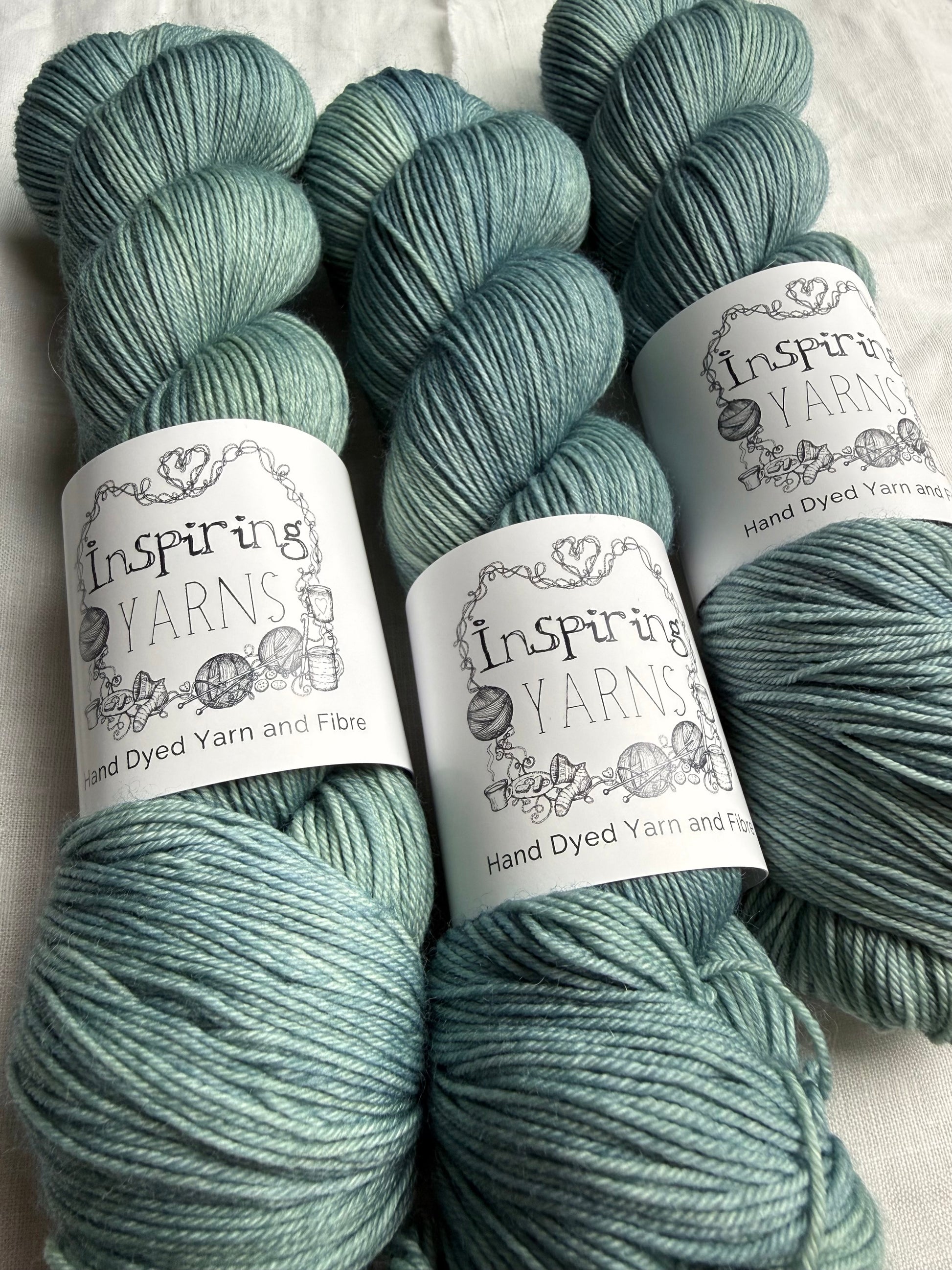 Three skeins of teal yarn with 'Inspire Yarns' labels on a white background