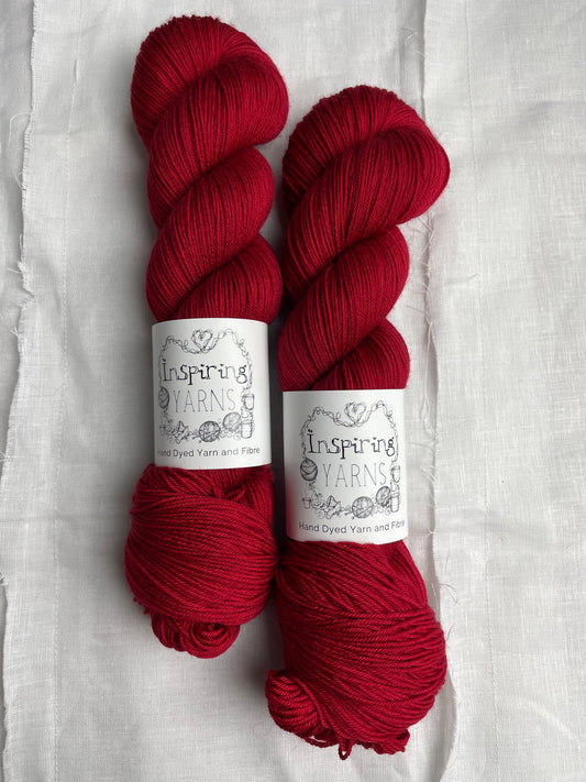 Two skeins of tonal blood red Merino Smooth Sock yarn labelled Inspiring Yarns on a white linen background