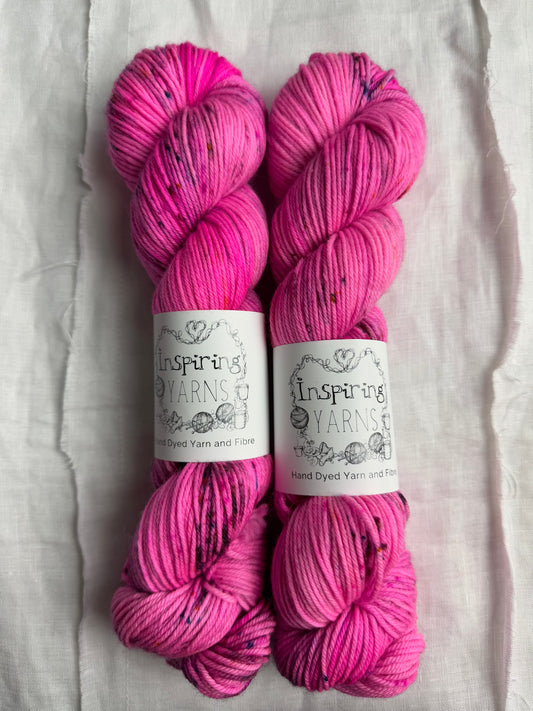 two skeins of neon pink yarn with speckles and inspiring yarns labels on a white background.