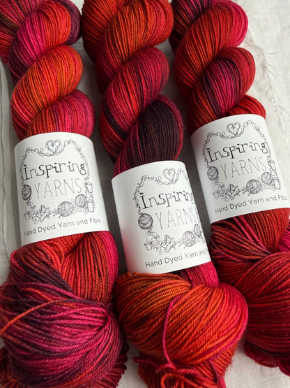 Close up of Three skeins of red variegated yarn labelled Inspiring Yarns on a white background