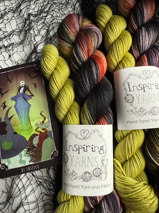 two Halloween sock sets with a small green skein and a large variegated skein. with a nightmare before Christmas card beside it.   on a black cobweb background. 