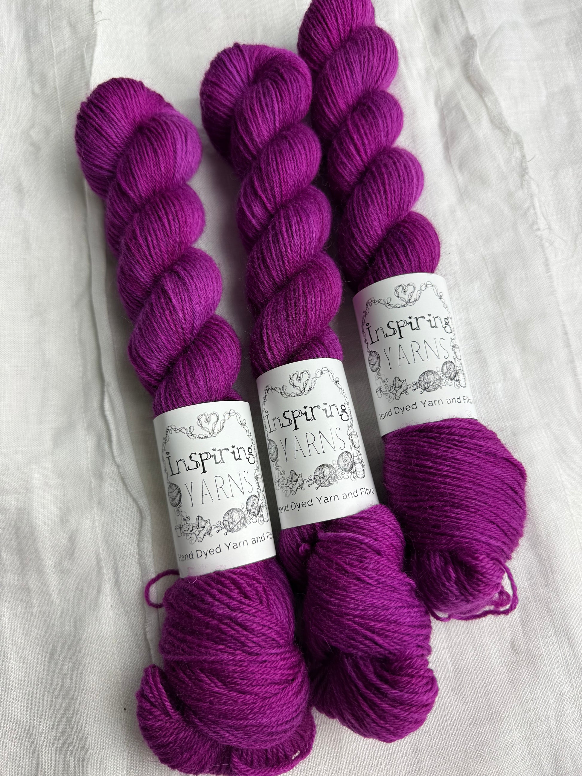 Three skeins of fuchsia tonal yarn labelled Inspiring Yarns on a white background