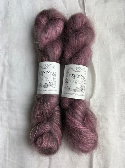 Two skeins of dusty purple yarn with labels on a white fabric background