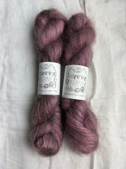 Two skeins of dusty purple yarn with labels on a white fabric background