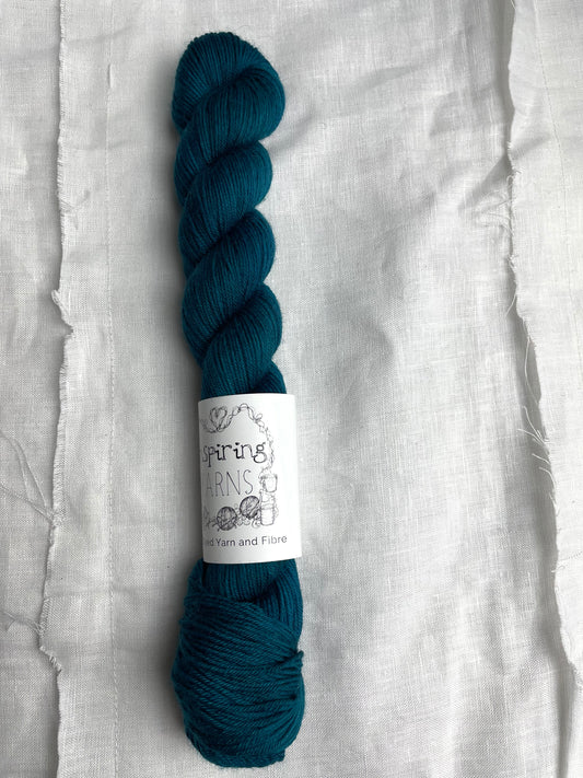 One intense teal blue coloured skeins of Merino Smooth Sock yarn branded  Inspiring Yarns on a white linen fabric background. 
