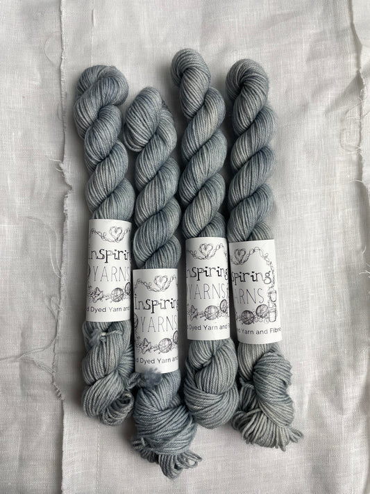 Four mini skeins of Ghost, a pale grey blue coloured Merino Smooth Sock, labelled Inspiring Yarns on a white linen background. 