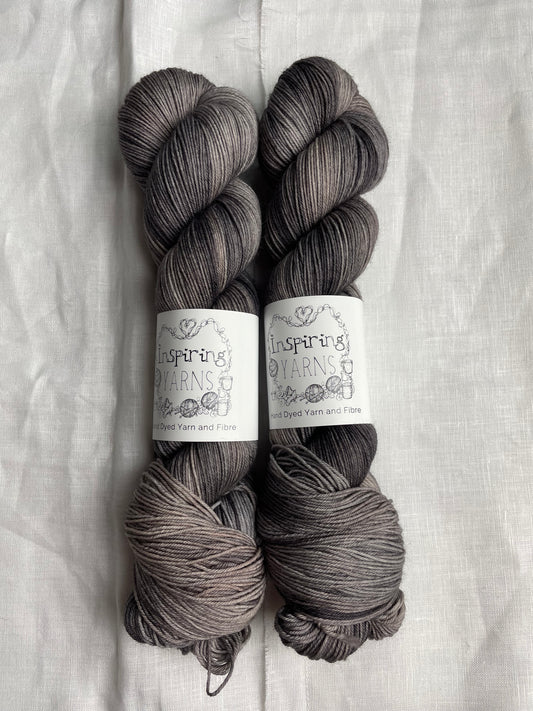 Two skeins of Merino Smooth Sock yarn hand dyed in a tonal grey colourway and labelled Inspiring Yarns on a white linen background.