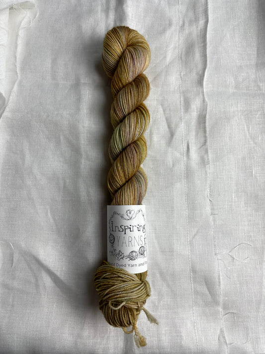 A skein of gold and pastel coloured hand dyed Merino Smooth Sock Yarn labelled Inspiring Yarns on a white linen background.