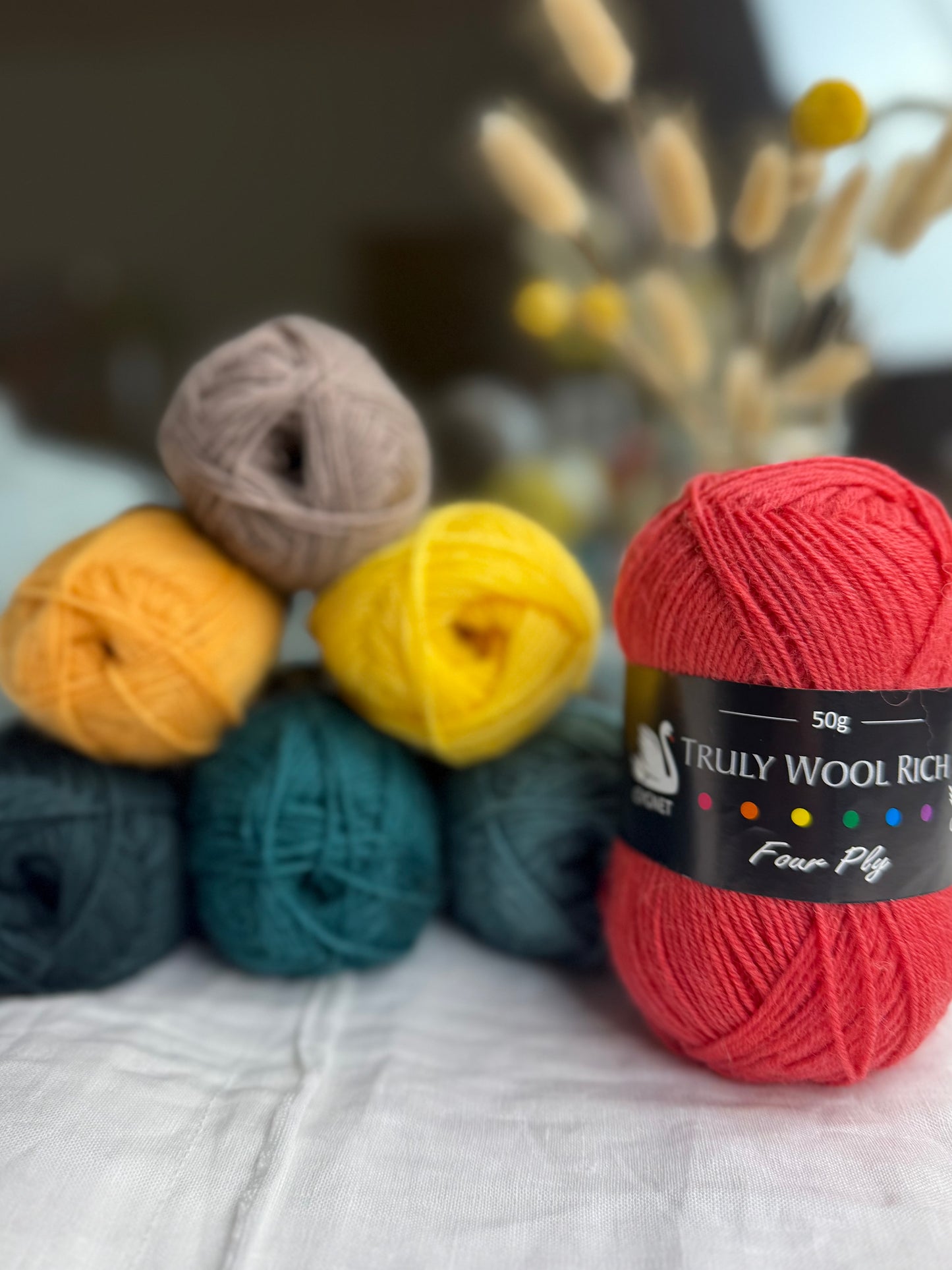 Colorful yarn balls with a red ball labeled 'Truly Wool Rich' on a textured surface.