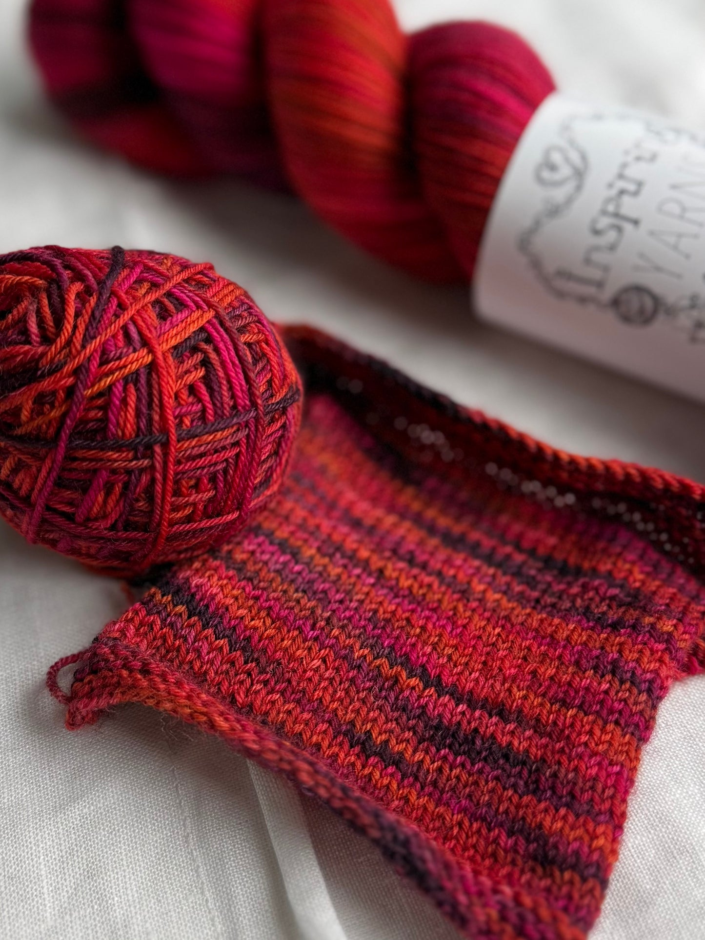 Knitted swatch with red orange pink and purple variegated yarn on a white background