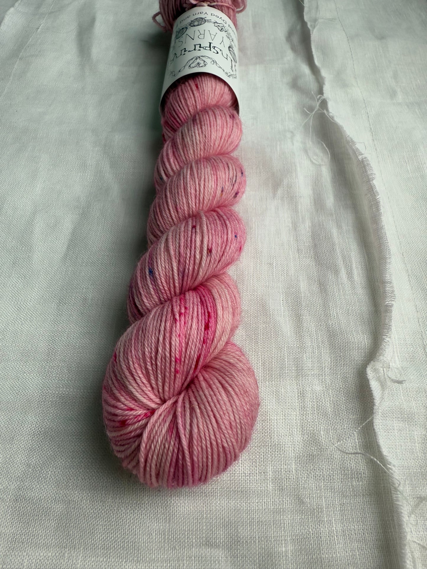up close of skein of dusty pink yarn with coloured speckles on a white background.