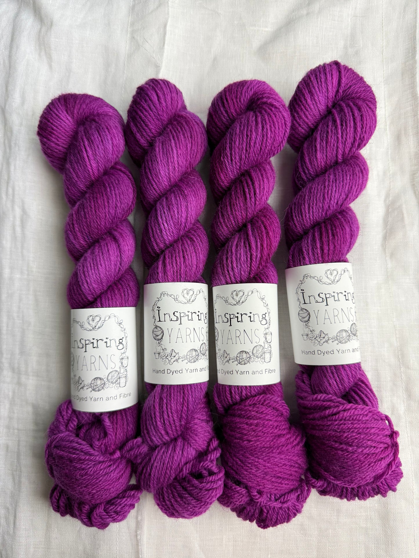Four skeins of fuchsia tonal yarn labelled Inspiring Yarns on a white background