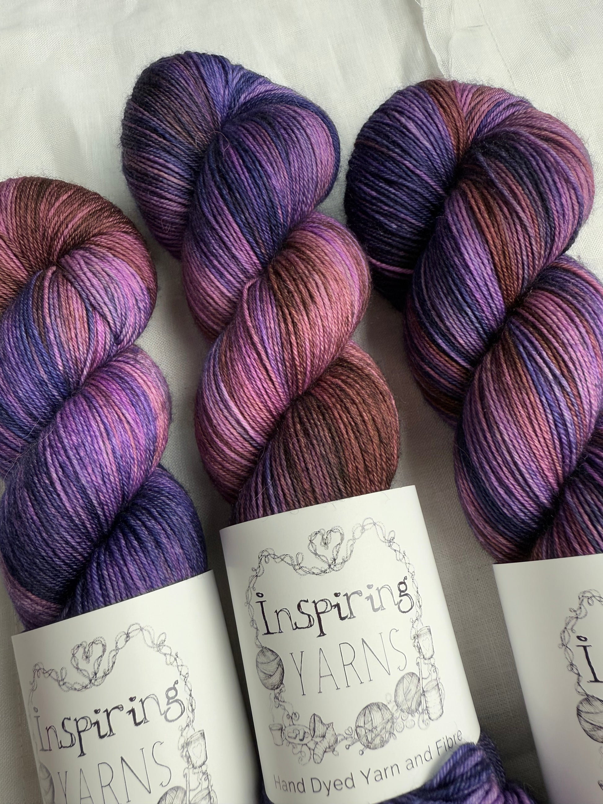 up close skeins of variegated yarn with purples, violets and browns. on white background and inspiring yarns label.