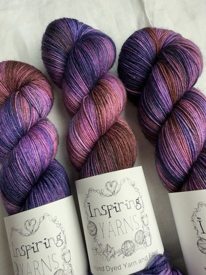 up close skeins of variegated yarn with purples, violets and browns. on white background and inspiring yarns label.
