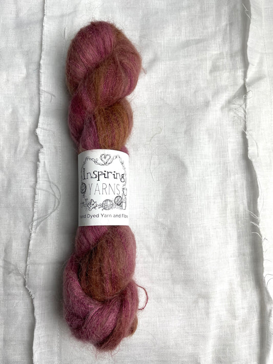 A skein of dusky pink Brushed Baby Suri  Silk lace yarn labelled Inspiring Yarns on a white linen background.