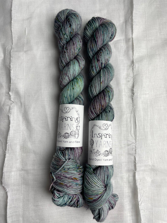 Two skeins of merino smooth sock yarn in a light teal colour with coloured speckles labelled Inspiring Yarns on a white linen background. 