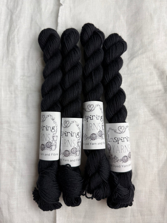 Four skeins of tonal charcoal black yarn with Inspiring Yarns labels on a white textured background.