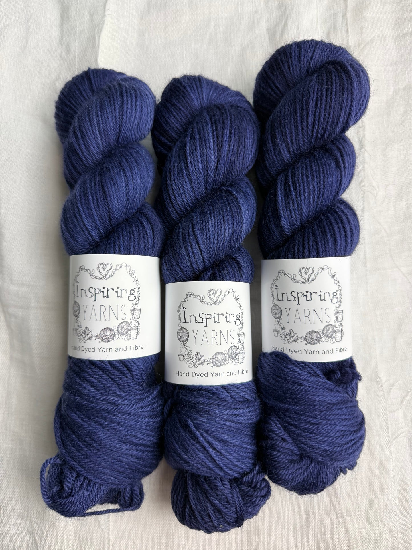 Three skeins of dark navy tonal yarn labelled Inspiring Yarns on a white background