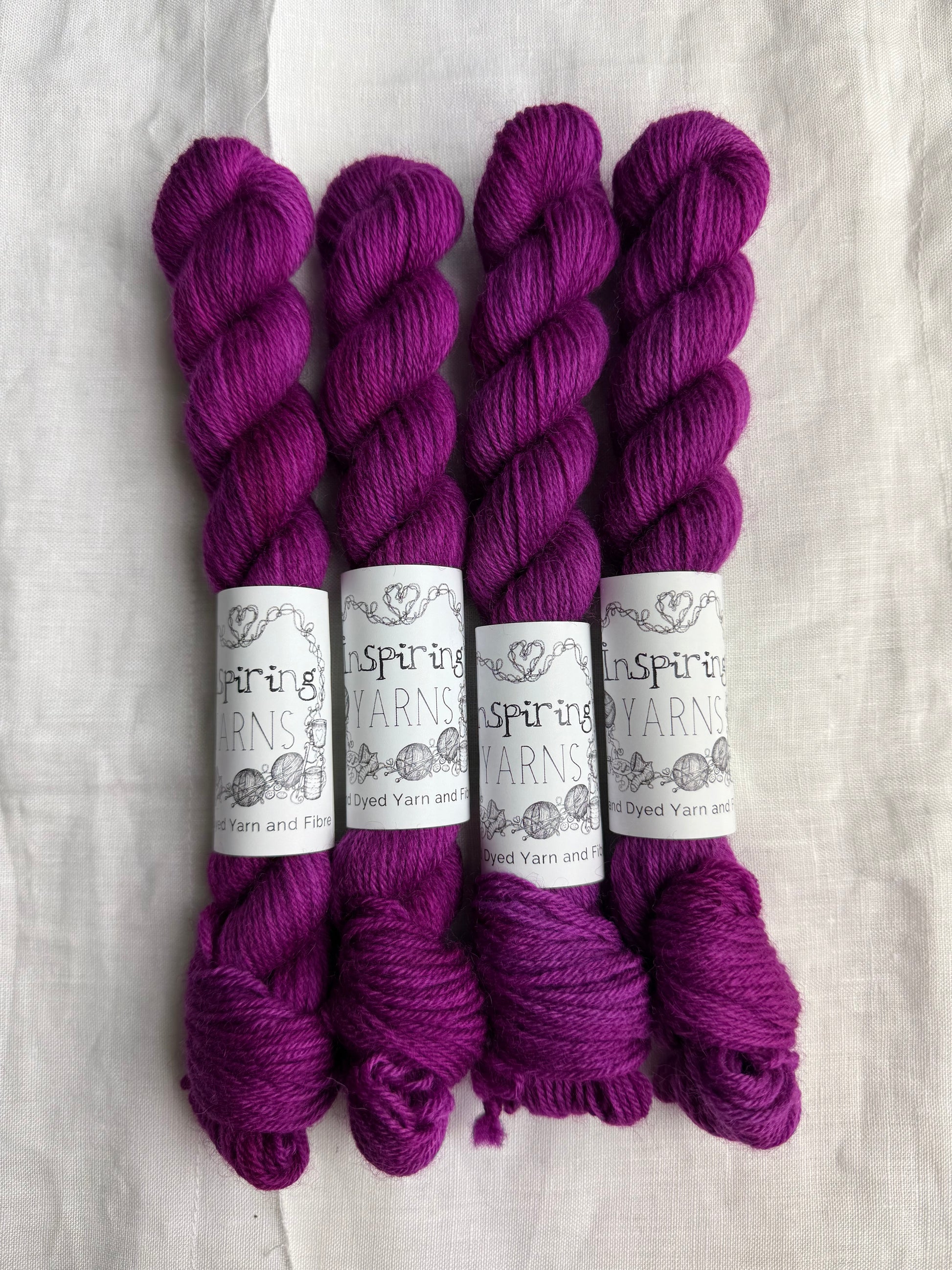 Four skeins of fuchsia tonal yarn labelled Inspiring Yarns on a white background