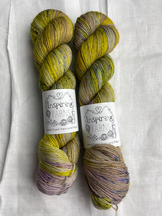 Two acid yellow and lilac coloured skeins of Merino Smooth Sock yarn branded  Inspiring Yarns on a white linen fabric background. 