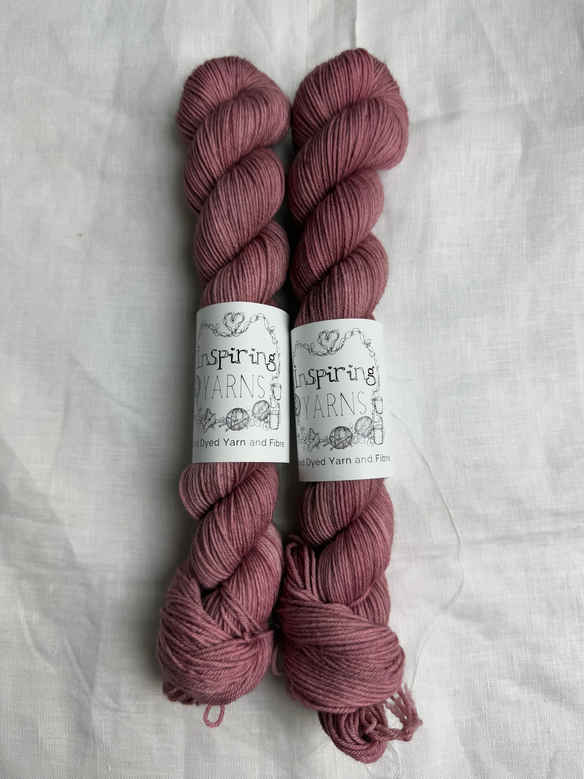 two skeins of dusty pink hand dyed yarn side by side on what background with inspiring yarns labels.
