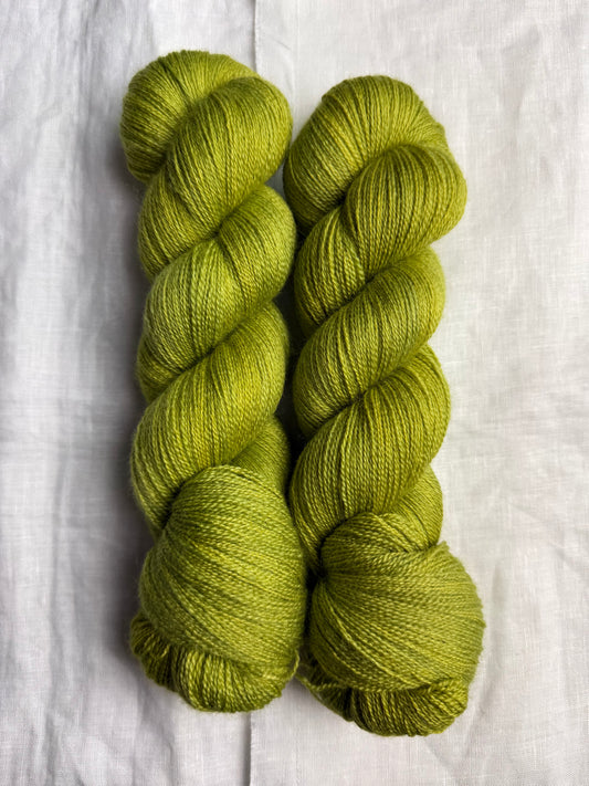 Two skeins of green yarn on a white fabric background