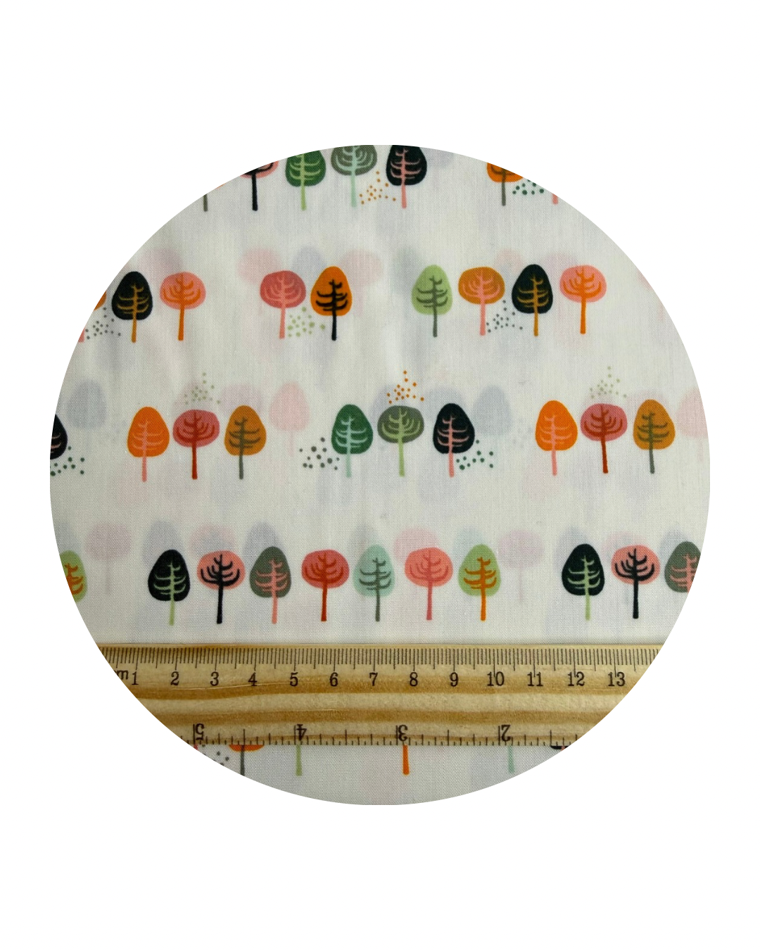 A circular swatch of Clear Path from the Lakeside Collection from Art Gallery Fabrics, a design of stylised small trees in rows in greens, oranges and pinks on a cream background and a wooden ruler in centimetres for scale on a white background.