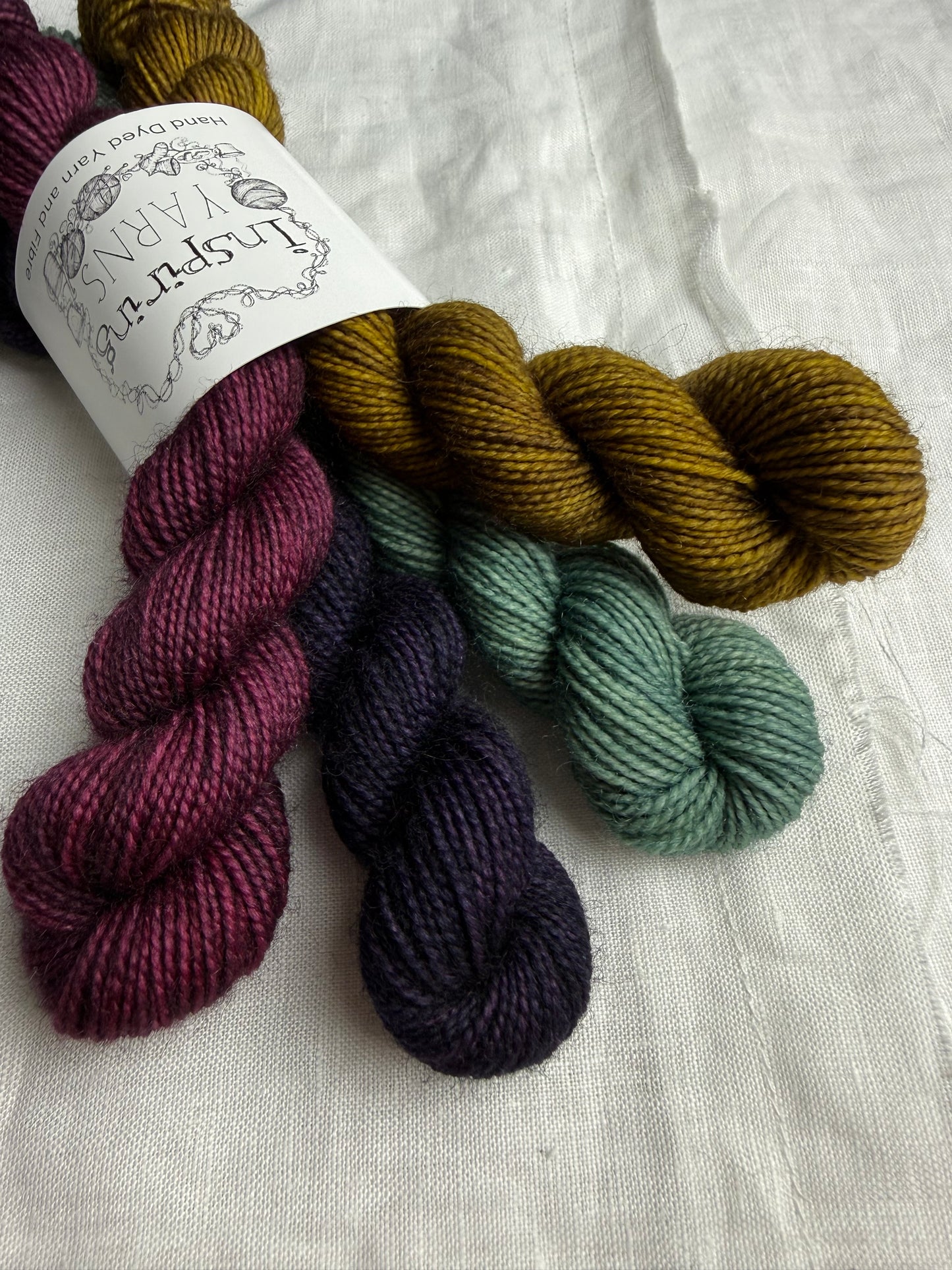 Bundle of 4 mini skeins of yarn labelled Inspiring Yarns on a white fabric background