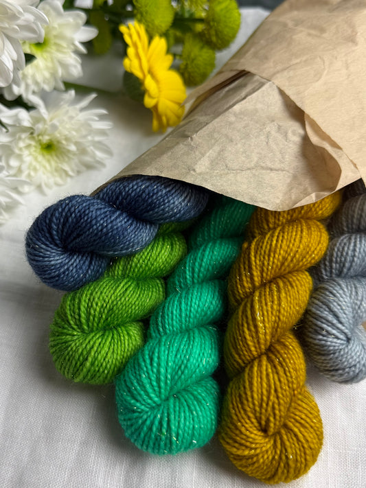 Set of colorful yarn skeins in a brown paper bag with flowers in the background