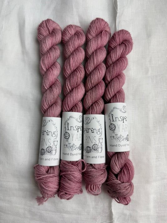 Four skeins of dusty pink yarn with inspiring yarn labels on a white fabric background.