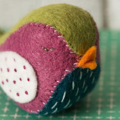 Felted toy resembling a bird on a green cutting mat. 