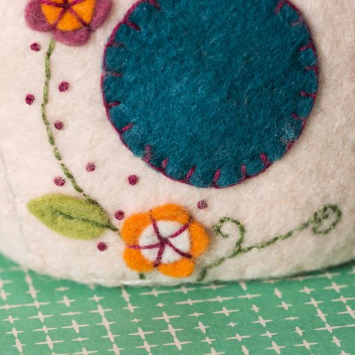 Close-up of a felt craft with embroidered flowers and a blue circle on a green grid background