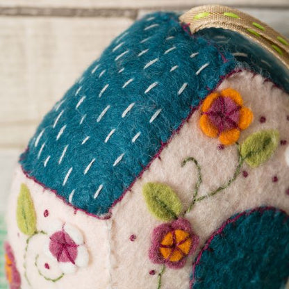 Felted fabric item with embroidered flowers and a blue roof on a neutral background. 