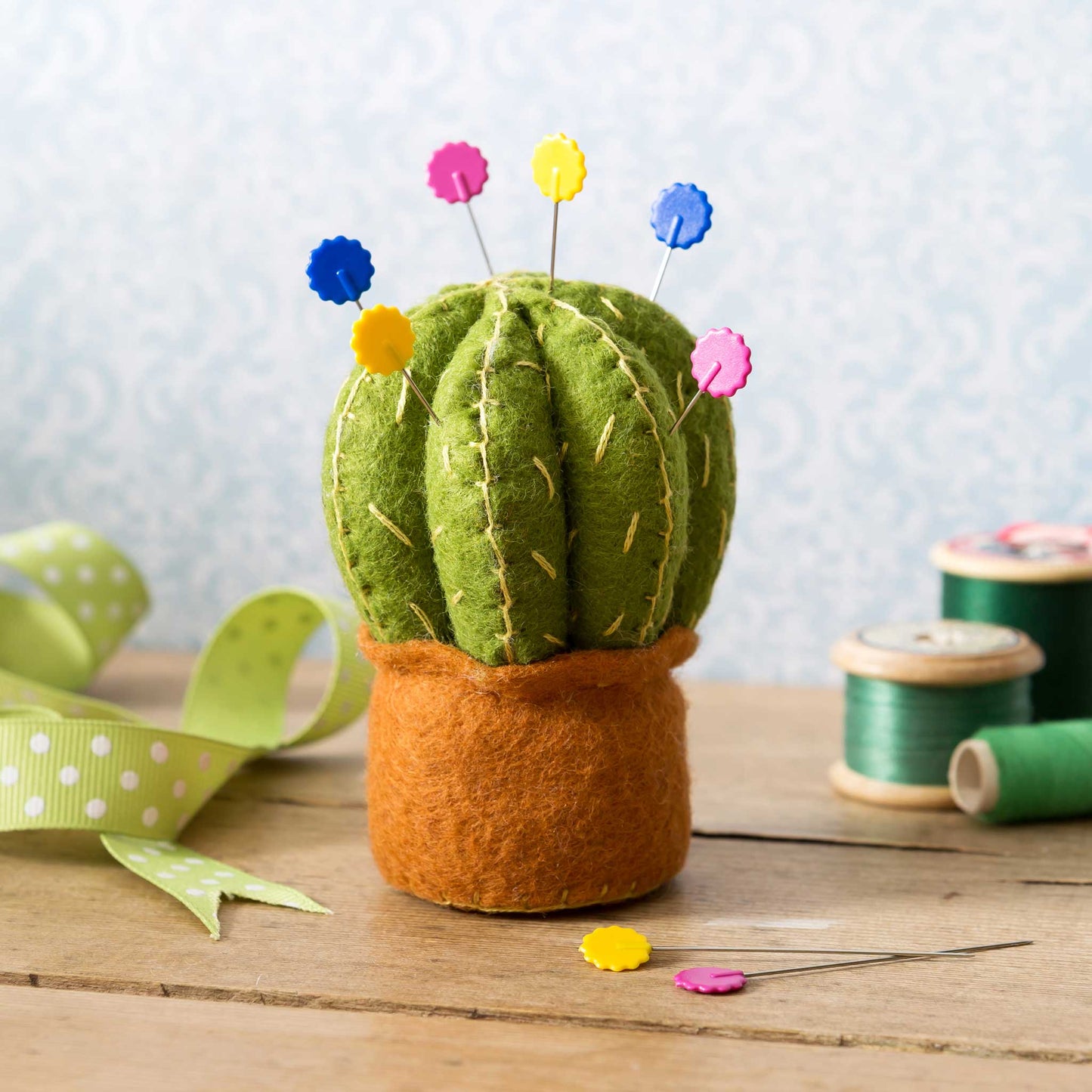 Felt cactus pincushion with colorful pins on a wooden surface