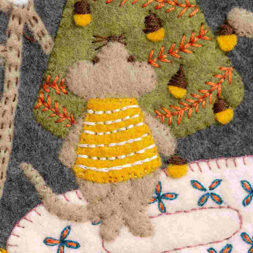 Close up of felt embroidery with a mouse wearing a yellow sweater and a tree.