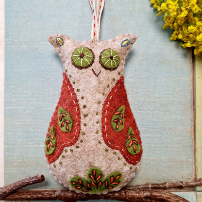 Felt owl ornament with red and green details on a branch against a light blue background